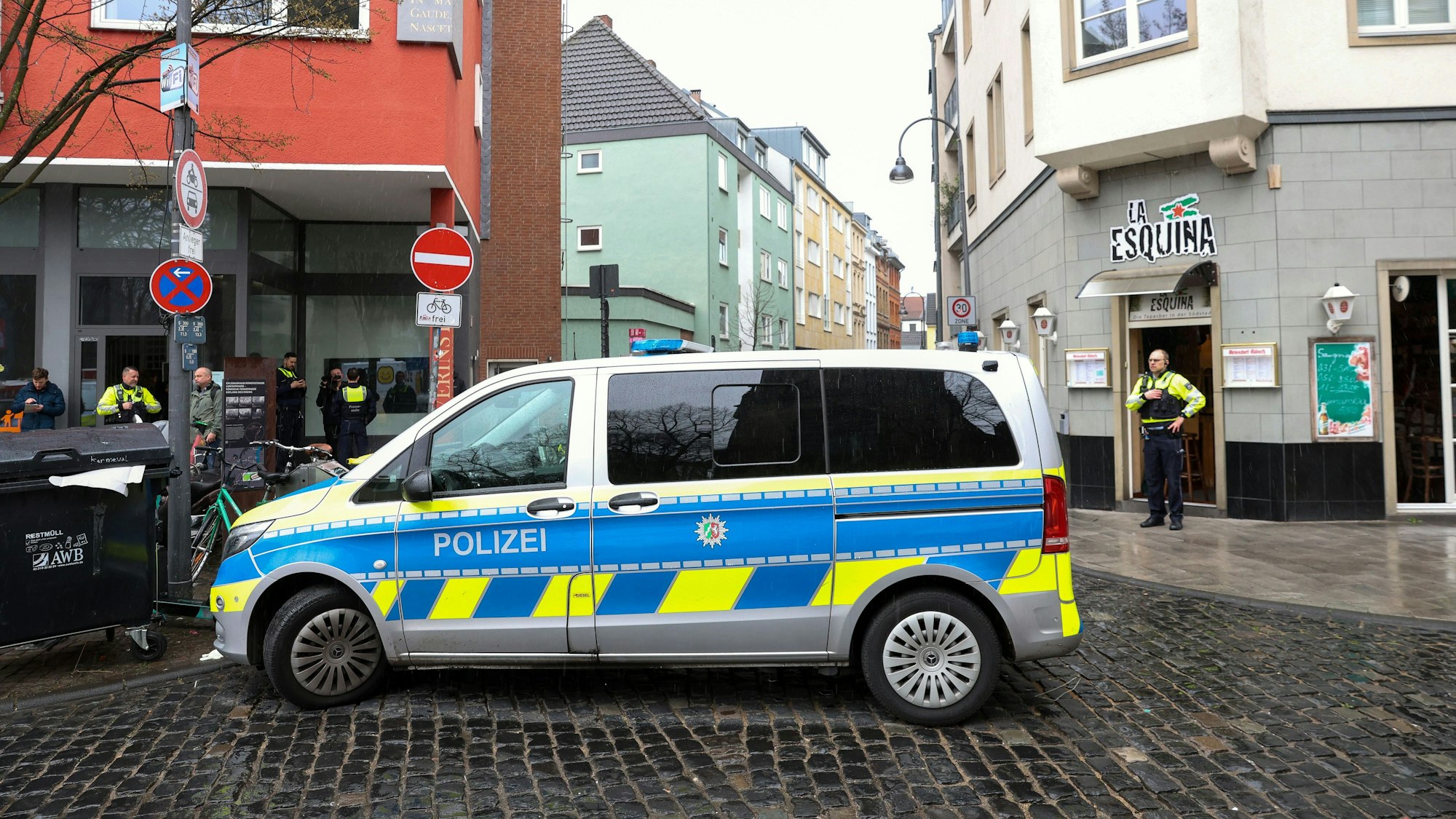 Polizei-Auto steht an einer Straße in Köln, im Hintergrund sind mehrere Einsatzkräfte und Privatpersonen zu sehen.
