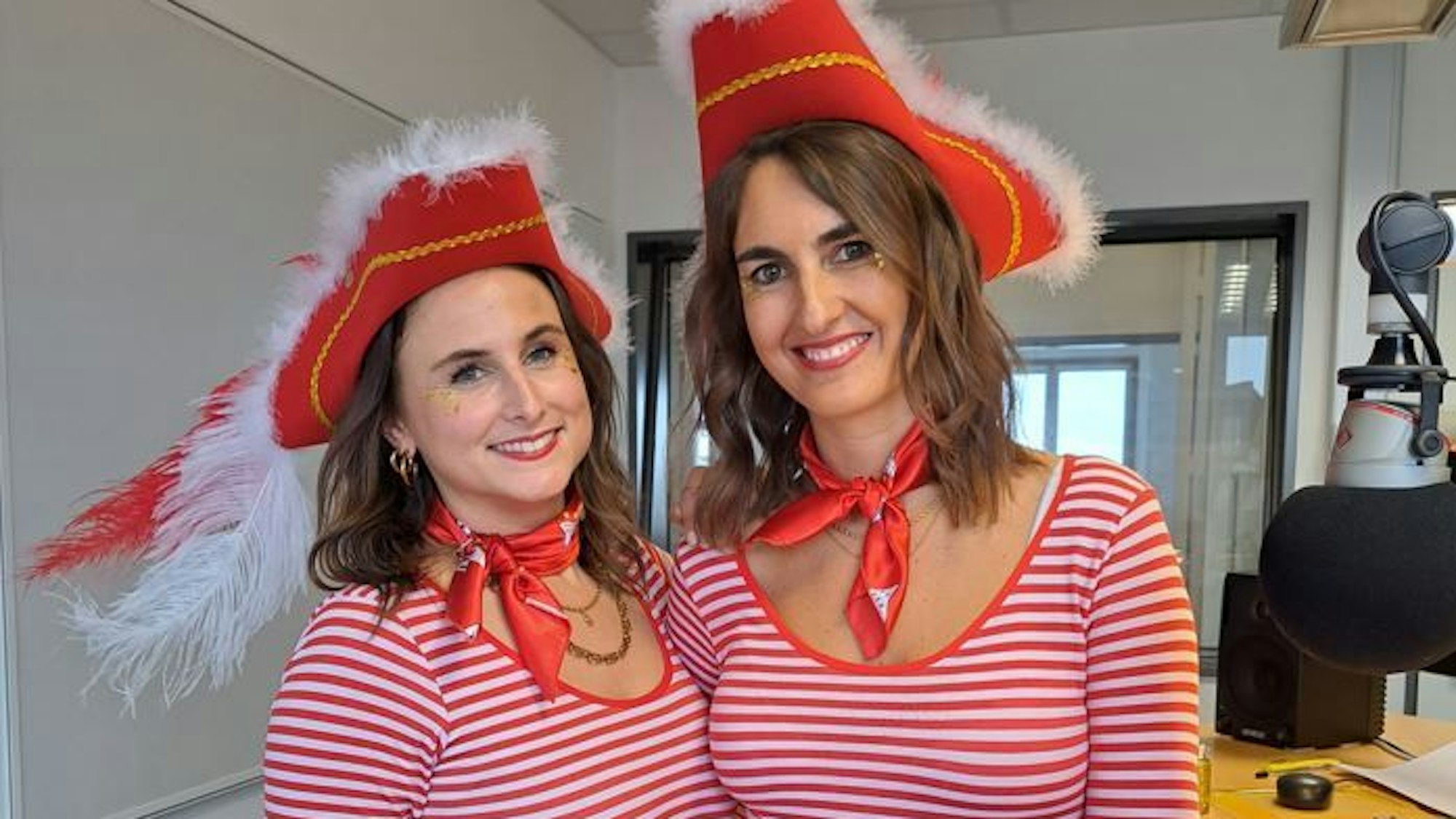 Zwei Frauen in rot-weißen Ringelshirts stehen in einem Studio und lächeln in die Kamera.