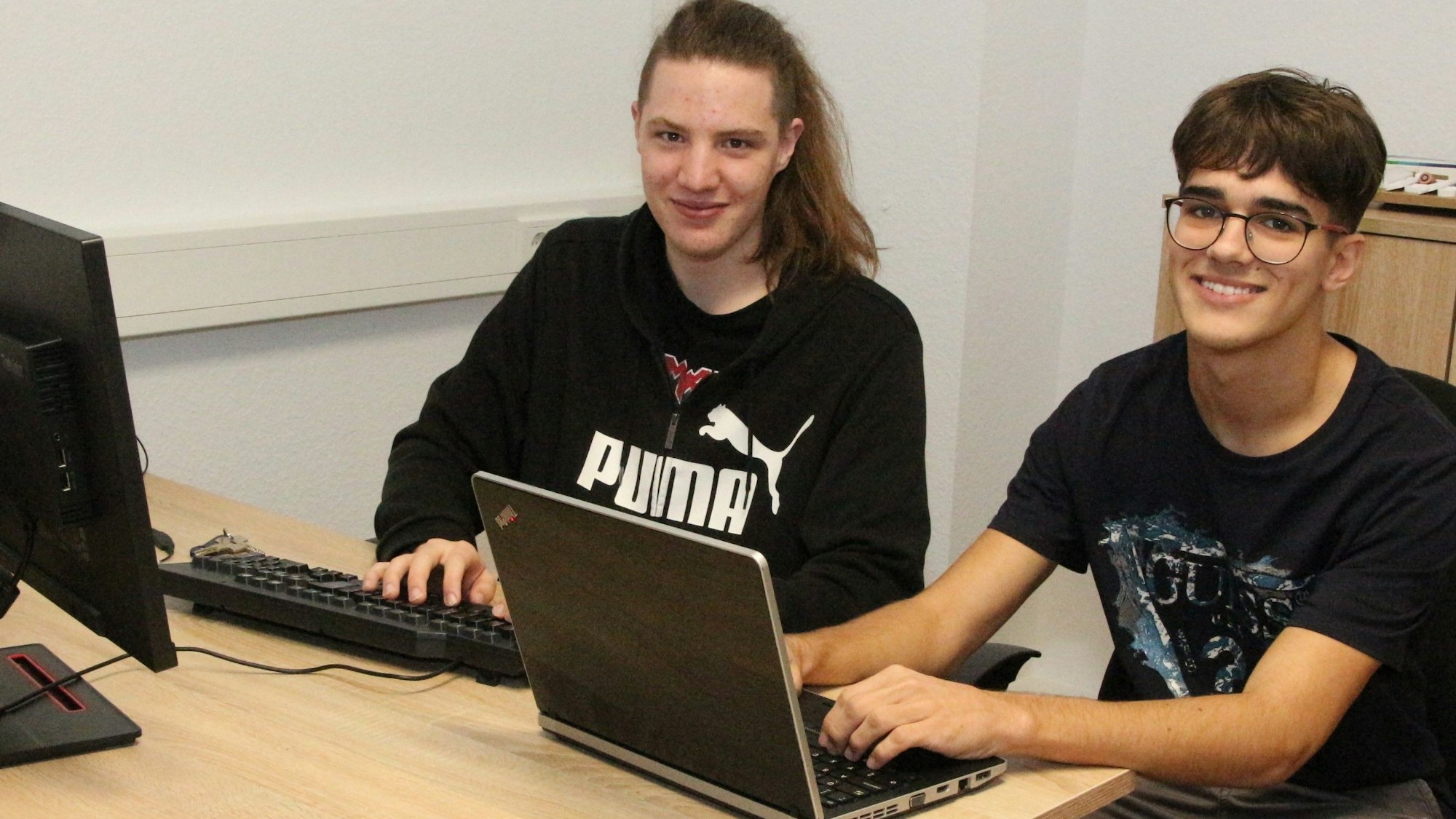 Aleksandar Kuraćević (r.) und Benjamin Bišćak kommen aus Slowenien und machen ein Praktikum im Unternehmen Lebensbaum in Lindlar. Sie sitzen an einem Schreibtisch nebeneinander und arbeiten an Laptops.