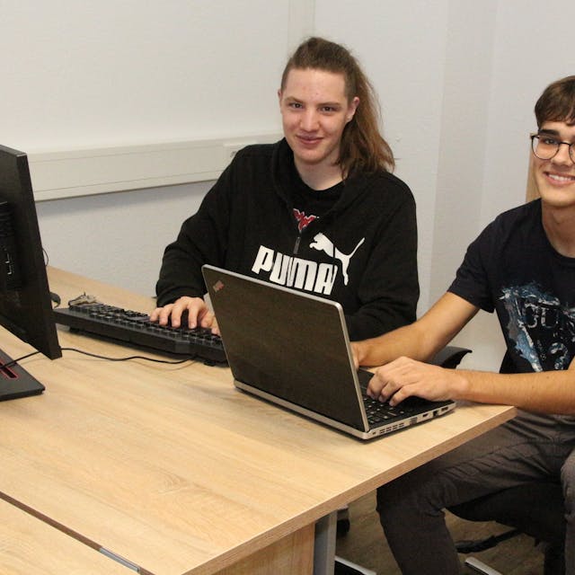 Aleksandar Kuraćević (r.) und Benjamin Bišćak kommen aus Slowenien und machen ein Praktikum im Unternehmen Lebensbaum in Lindlar. Sie sitzen an einem Schreibtisch nebeneinander und arbeiten an Laptops.