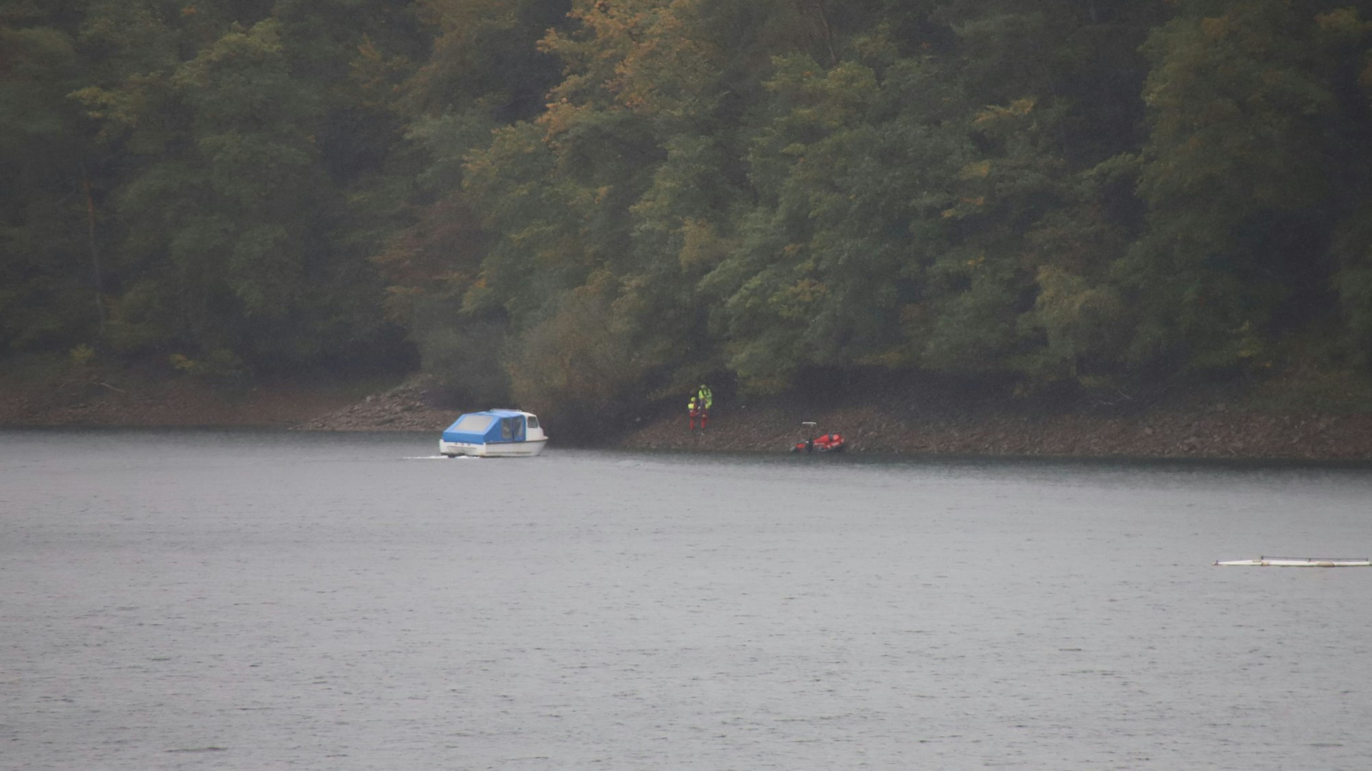 Ein Boot steht an einem Ufer. An dem Ufer stehen Rettungskräfte.