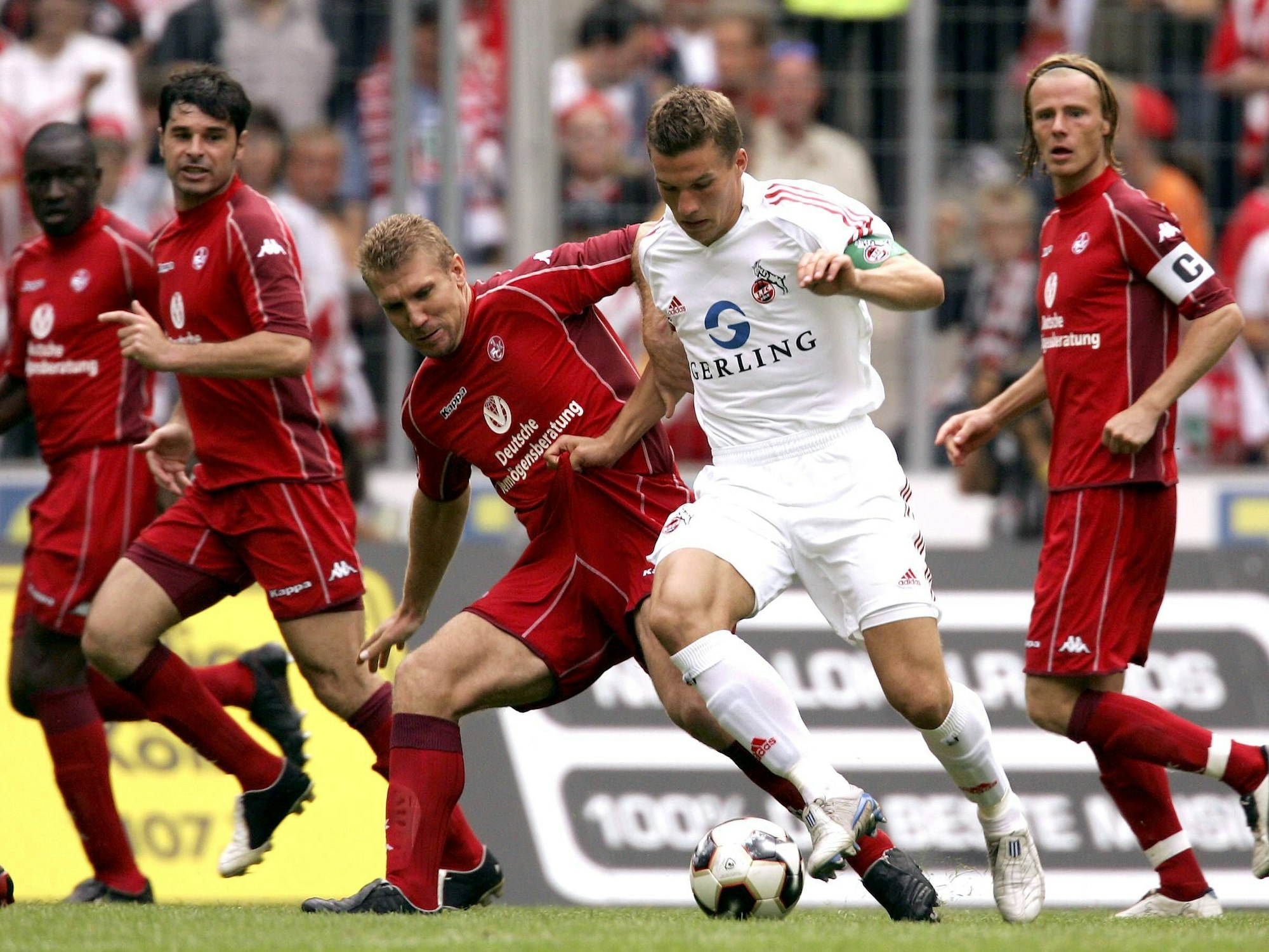 Lukas Podolski, mit Kapitänsbinde, dribbelt mehrere Kaiserslauternspieler aus.