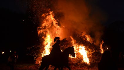 Ein Martins-Darsteller reitet im Dunkel mit einem römischen Helm auf einem Pferd vor einem Feuer.