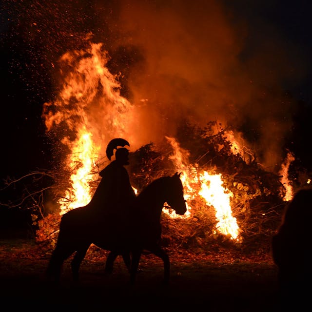 Ein Martins-Darsteller reitet im Dunkel mit einem römischen Helm auf einem Pferd vor einem Feuer.