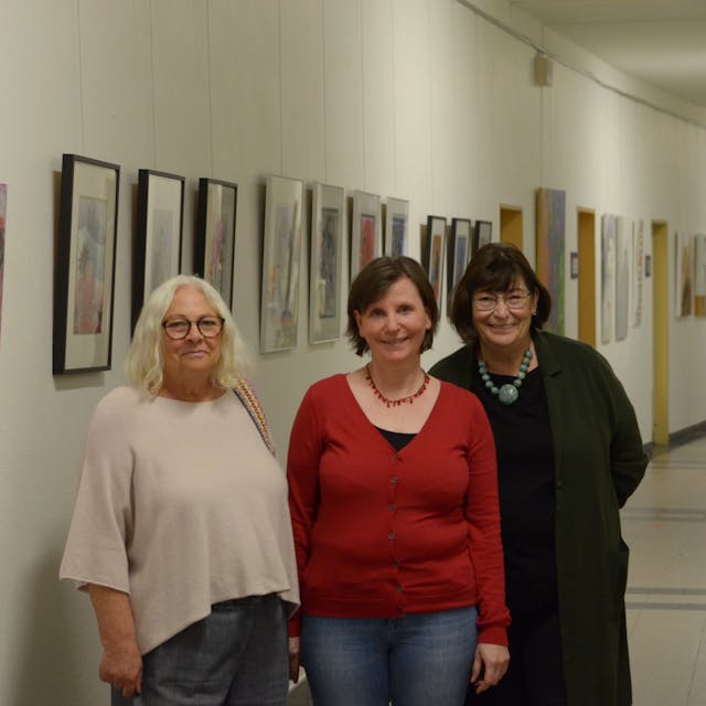 Die Künstlerinnen Donata Reinhard (v.l.), Petra Hansen und Beate Krupp stehen in einem der Flure des Euskirchener Rathauses, in denen sie ihre Werke ausstellen. Im Hintergrund hängen zahlreiche Bilder.