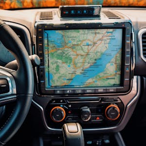 Illustration: Innenansicht eines Autos mit Blick durch die Windschutzscheibe, Lenkrad, Armaturenbrett, Navigationsgerät.
