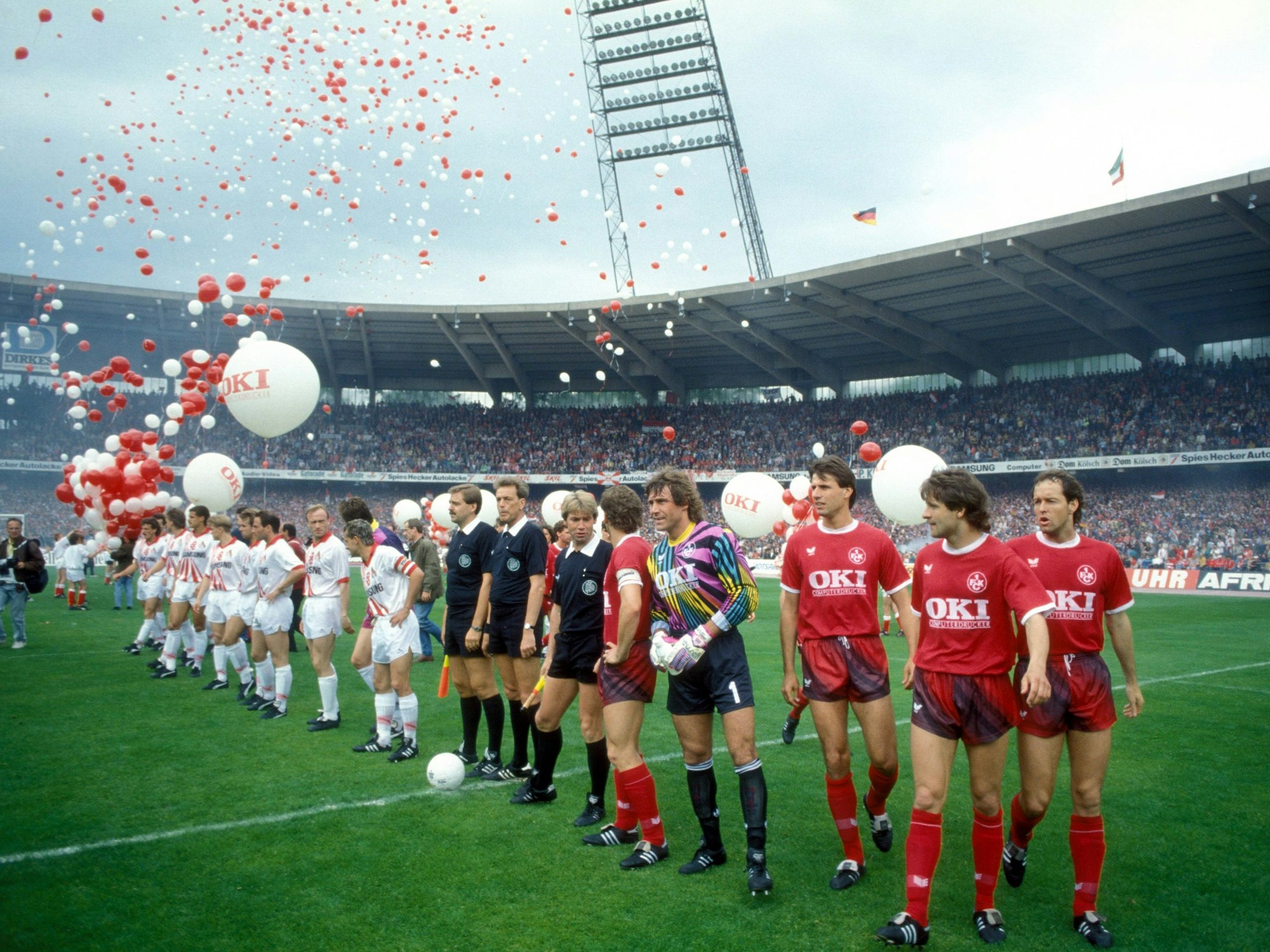 Die Spieler der Mannschaften von Kaiserslautern und Köln stellen sich vor dem Spiel im Müngersdorfer Stadion auf. Ballons in Rot und Weiß fliegen in die Luft.