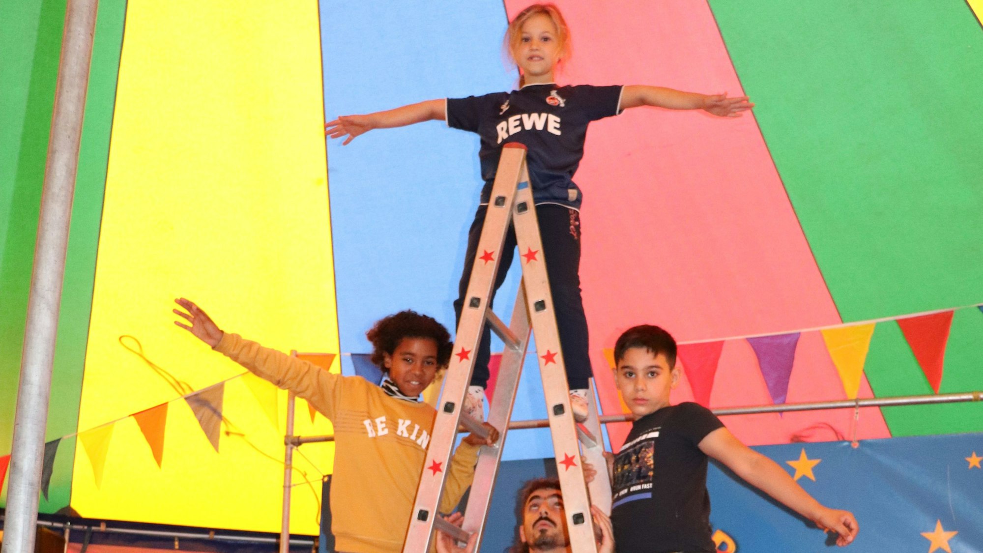 Kinder stehen auf einer Leiter unter der bunten Zirkuszelt-Kuppel.