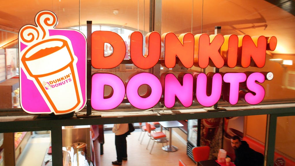 Das Firmenlogo klebt an der Fensterscheibe einer Filiale der amerikanischen Donut-Kette Dunkin' Donuts, aufgenommen in Berlin.