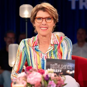 Moderatorin Bettina Böttinger sitzt im Studio des „Kölner Treff“. Sie trägt eine bunt gemusterte Bluse und blickt lächelnd in die Kamera.