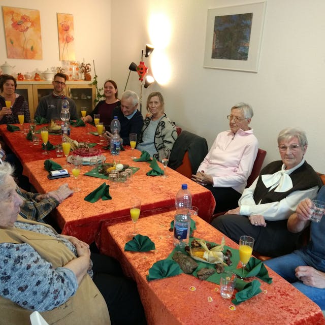 Seniorinnen und Senioren sitzen an einem Tisch und prosten sich zu.
