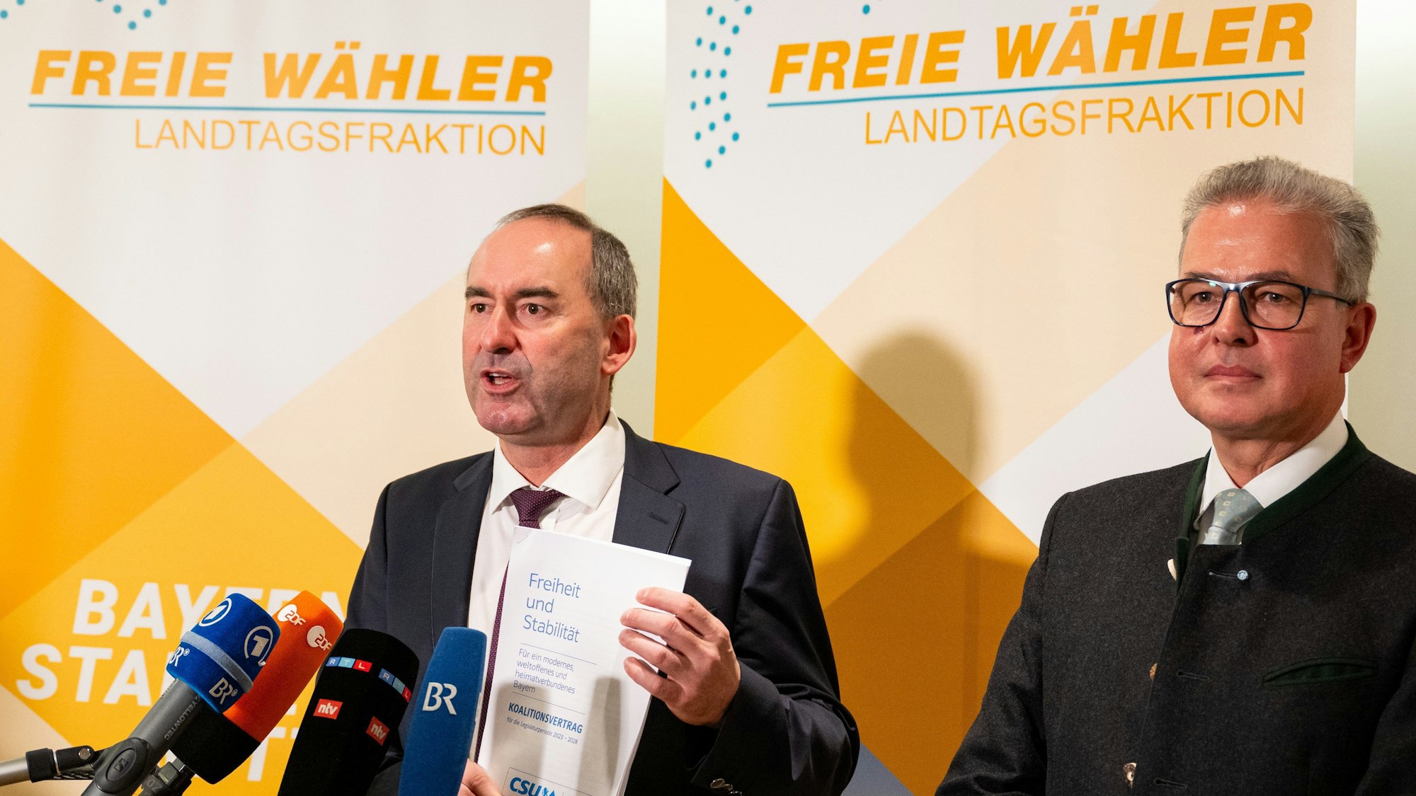 Freie-Wähler-Chef Hubert Aiwanger (l) präsentiert den unterschriebenen Koalitionsvertrag mit der CSU. Die Affäre um das antisemitische Flugblatt nimmt indes eine Wendung, Ermittler nehmen den Hinweisgeber ins Visier.
