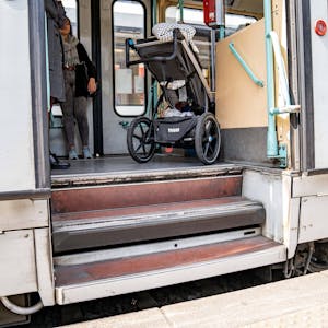 Das Foto zeigt einen Straßenbahnausstieg mit zwei Stufen. Vor der oberen Stufe steht ein Kinderwagen. Für Kinderwagen und Menschen im Rollstuhl sind derartige Ausstiege aus öffentlichen Verkehrsmitteln nur schwer zu bewältigen.&nbsp;