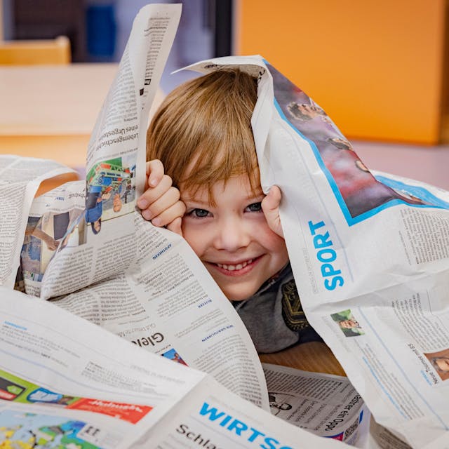 Ein kleiner Junge umgeben von Zeitungsseiten der Bonner Rundschau.&nbsp;