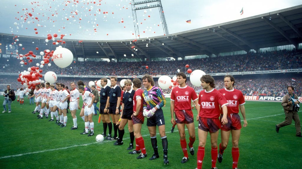 Die Spieler der Mannschaften von Kaiserslautern und Köln stellen sich vor dem Spiel im Müngersdorfer Stadion auf. Ballons in Rot und Weiß fliegen in die Luft.