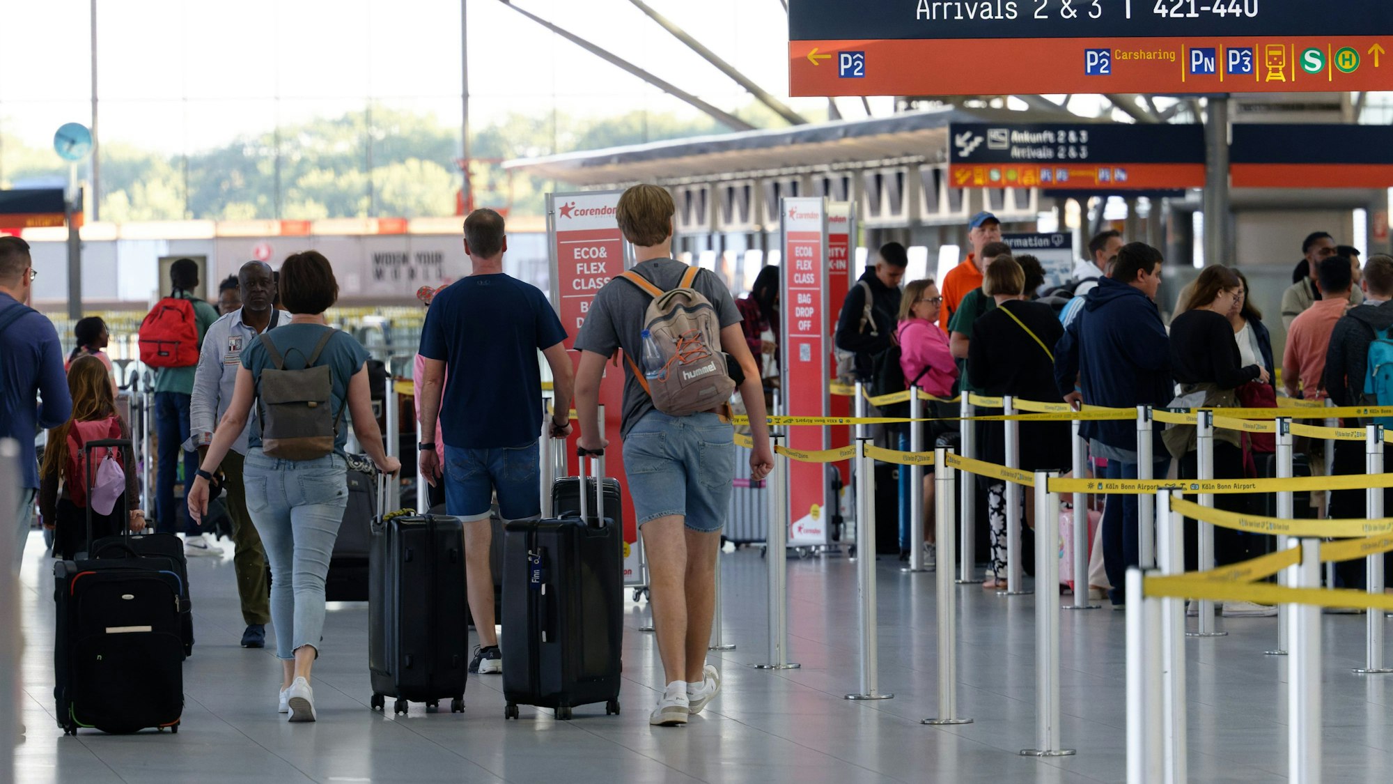 Reisende am Flughafen Köln/Bonn gehen mit ihrem Gepäck durch die Abflughalle.