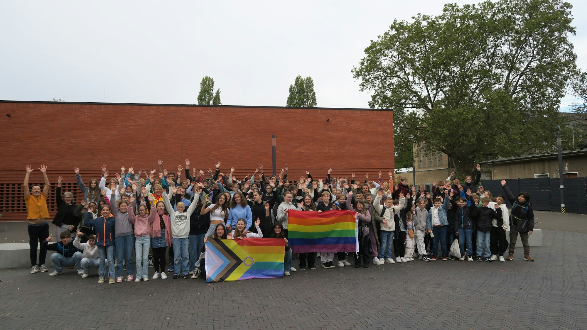 Eine Menge von Schülerinnen und Schülern hat sich auf einem Schulhof zum Foto aufgestellt, sie haben zwei bunte Flaggen bei sich.
