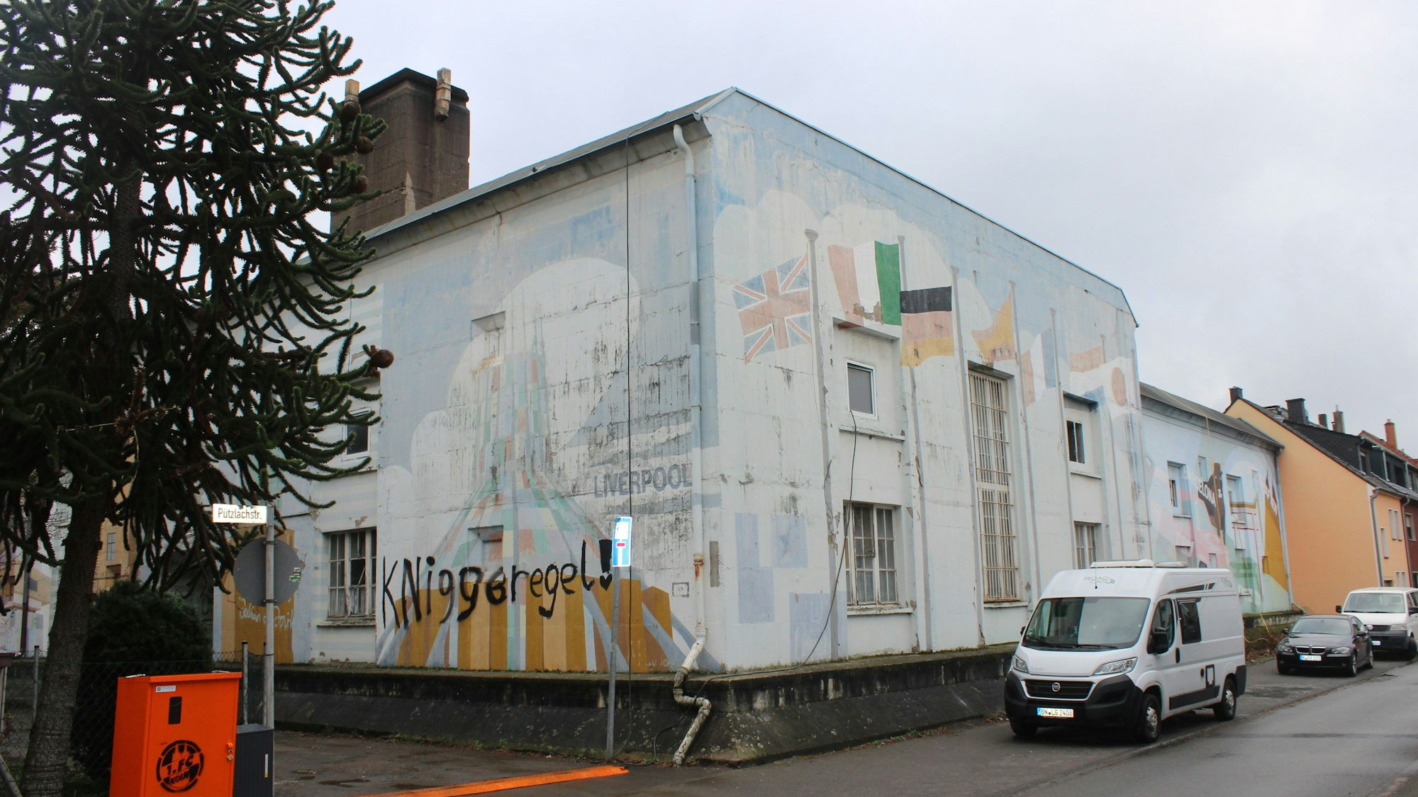 Ein würfelförmiges mit Graffiti besprühtes Gebäude steht an einer Straßenecke.