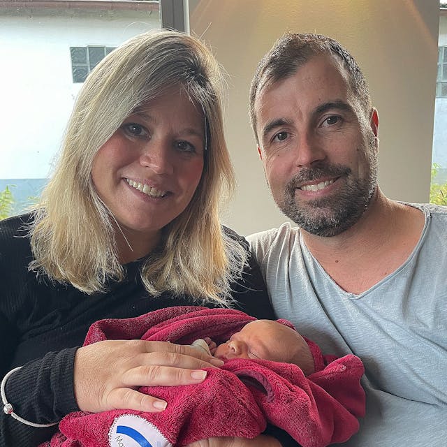 Jennifer und Krishan Meuren halten ihren neugeborenen Sohn Levi in einer roten Decke im Arm.