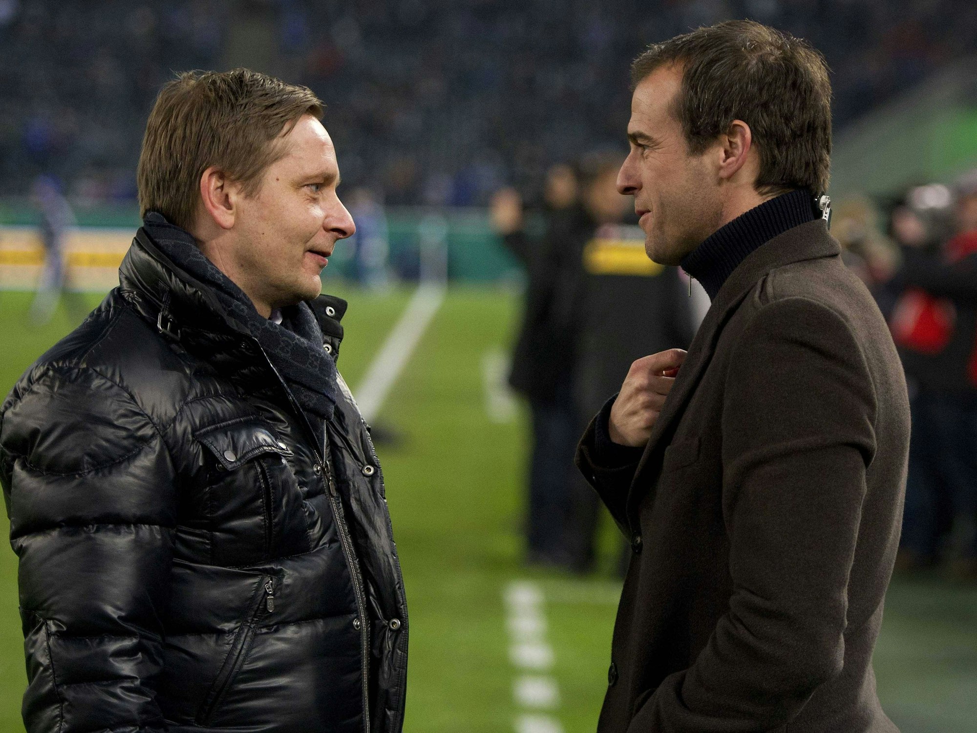 Horst Heldt und Mehmet Scholl unterhalten sich am Spielfeldrand.