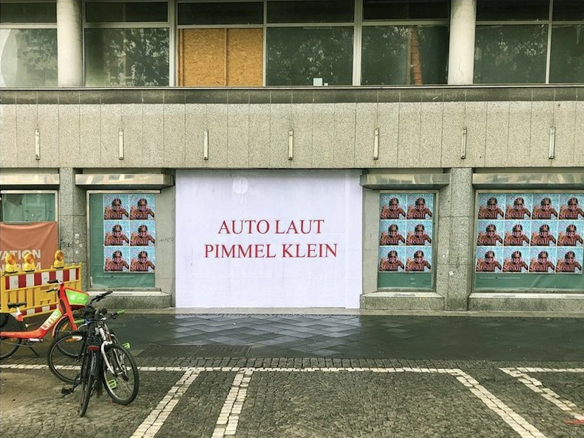 Ein Plakat mit der Aufschrift Auto laut, Pimmel klein ist auf den Kölner Ringen zu sehen.
