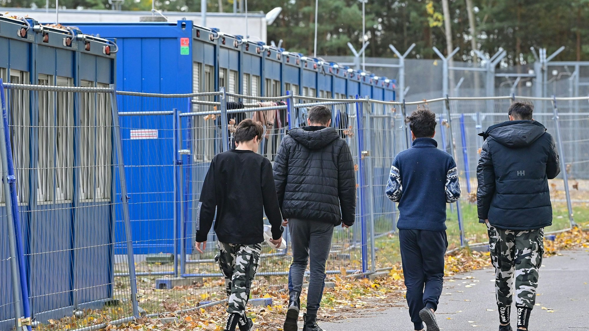 Vier Jugendliche sind von hinten zu sehen, daneben stehen Container für Geflüchtete