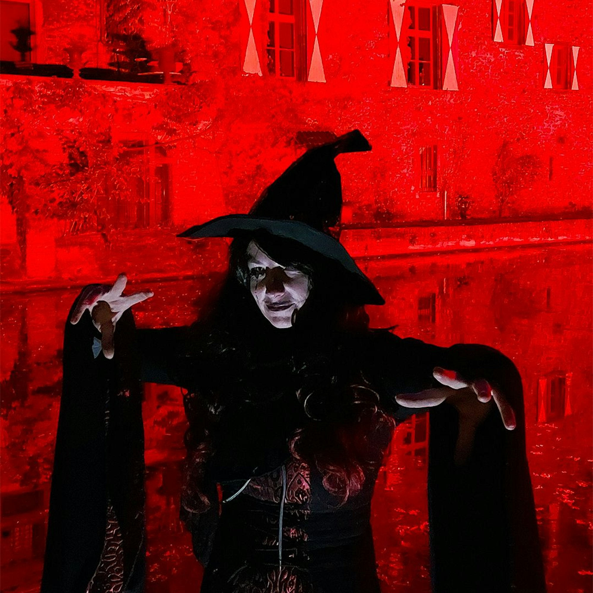 Als Hexenzauberin lauert die Frau vor der rot illuminierten Burg.
