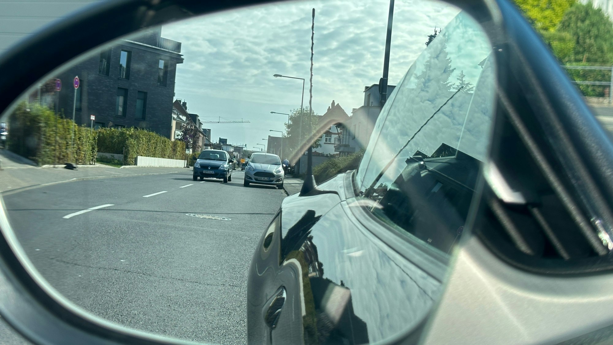 Im Rückspiegel ist ein Auto zu sehen, das ein parkendes Auto überholt.