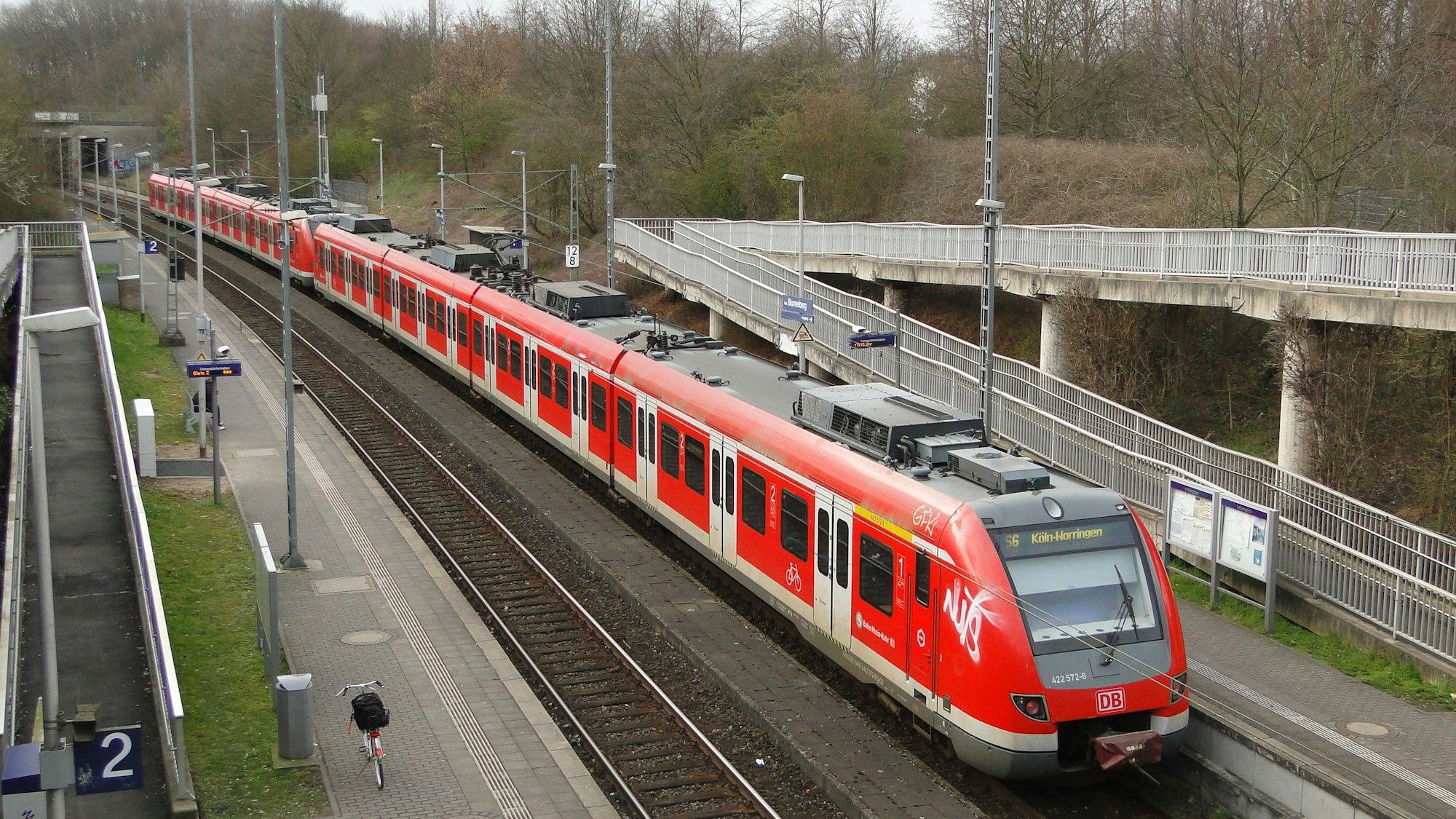 Eine S-Bahn steht an einer Haltestelle, die durch eine Fußgängerbrücke erreichbar ist.