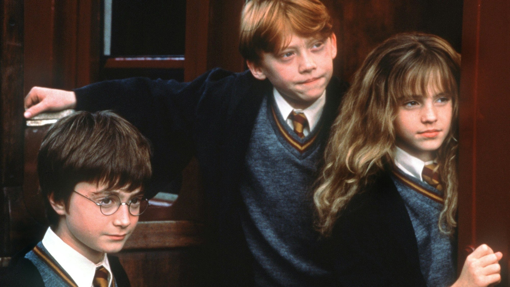 Harry Potter (Daniel Radcliffe, l.), Ron Weasley (Rupert Grint) und Hermine Granger (Emma Watson) stehen im Kinofilm „Harry Potter und der Stein der Weisen“ an der Tür zur Hogwarts-Schule für Zauberkunst.