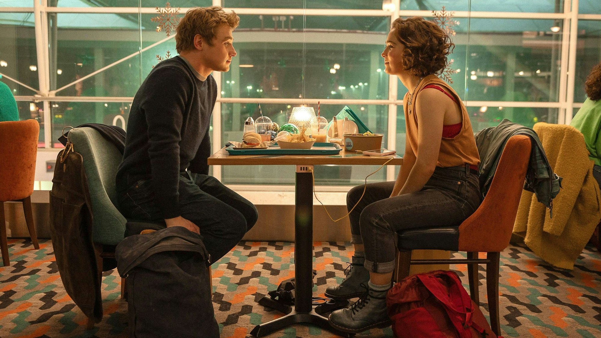 Szenenfoto aus „Die statistische Wahrscheinlichkeit von Liebe auf den ersten Blick“: Hadley (Hayley Lu Richardson) und Oliver (Ben Hardy) sitzen sich gegenüber am Flughafen.