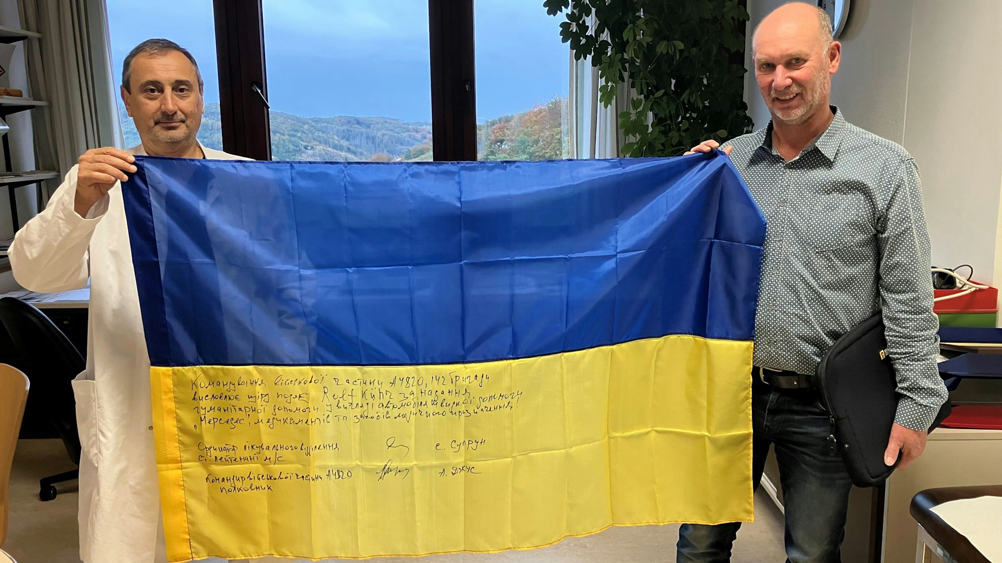 Zwei Männer halten eine Ukraine-Flagge in den Händen. Darauf ist eine Dankesbotschaft in ukrainischer Sprache geschrieben.