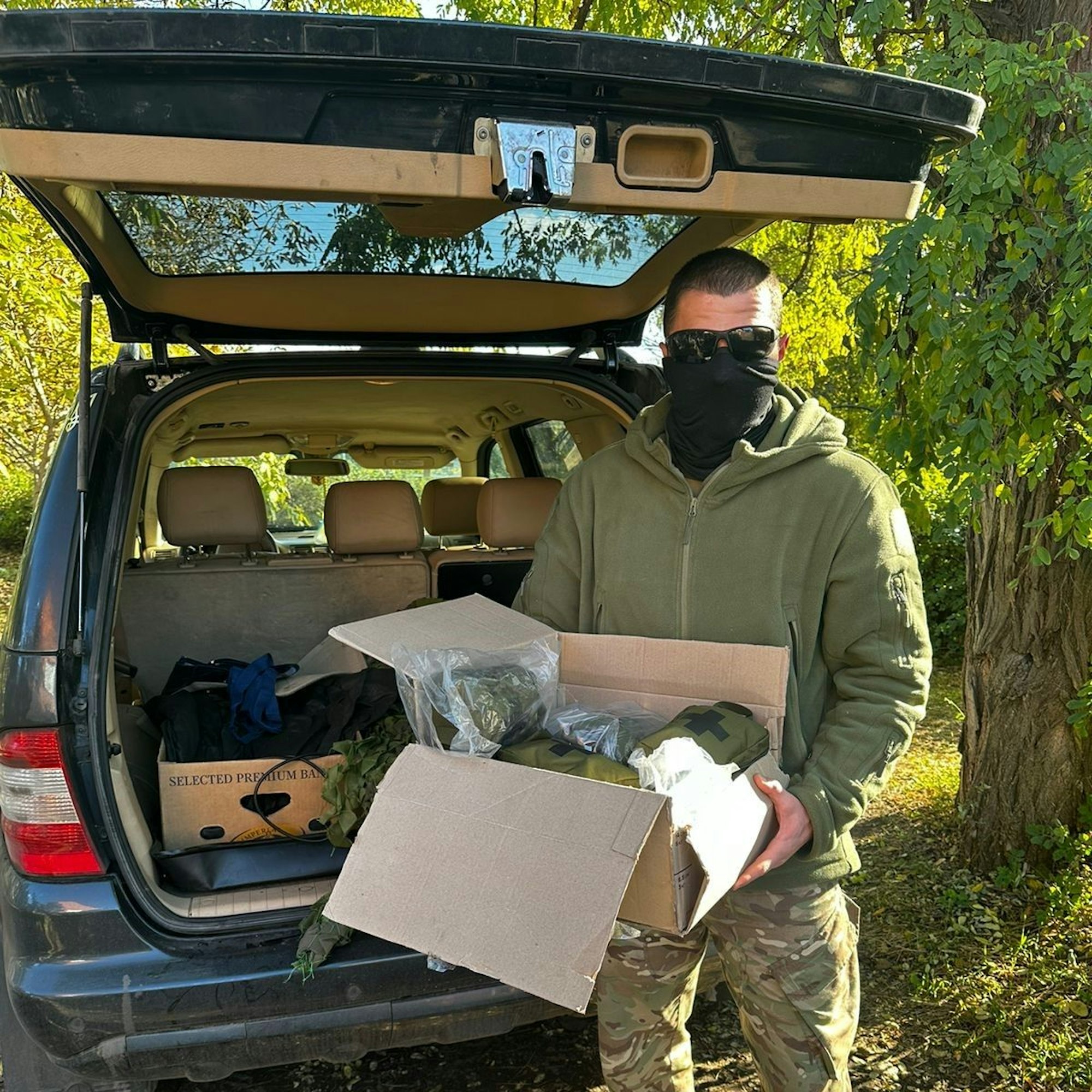 Ein vermummter Soldat mit Sonnenbrille hält ein Paket mit medizinischen Hilfsmitteln in der Hand.