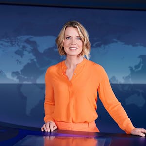 Tagesthemen-Moderatorin Jessy Wellmer steht im ARD-Nachrichtenstudion in Hamburg und schaut in die Kamera. Sie trägt eine orangefarbene Hose und ein orangefarbenes Oberteil.