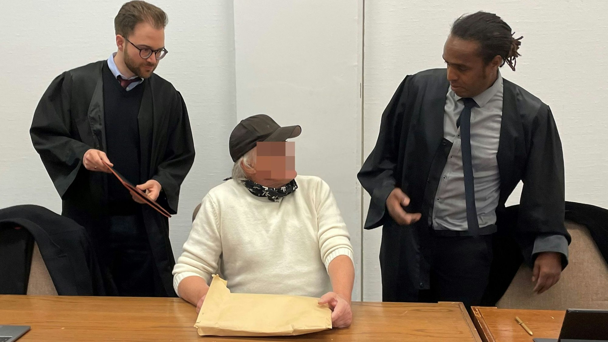 Ein Mann mit Basecap sitzt auf der Anklagebank, rechts und links von ihm steht jeweils ein Anwalt.