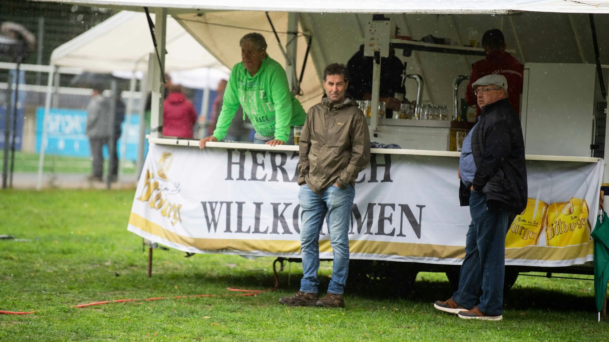 Das Bild zeigt zwei Fans, die dem Regen beim kleinen Pokalfinale trotzen. Sie stehen an einer Bierbude.