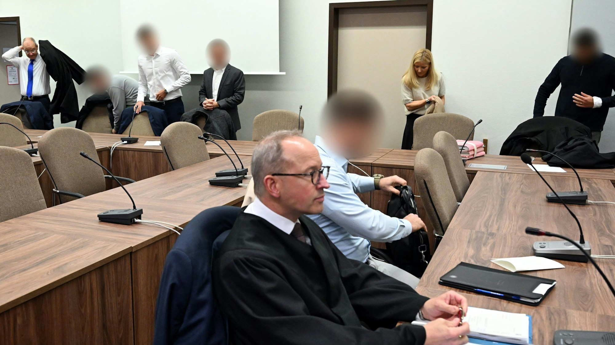 Zu sehen ist das Innere eines Gerichtsgebäudes in Köln. Die Angeklagten warten mit ihren Rechtsanwälten auf den Beginn des Prozesses.