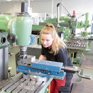 Eine junge Frau stellt eine Fräsmaschine ein.