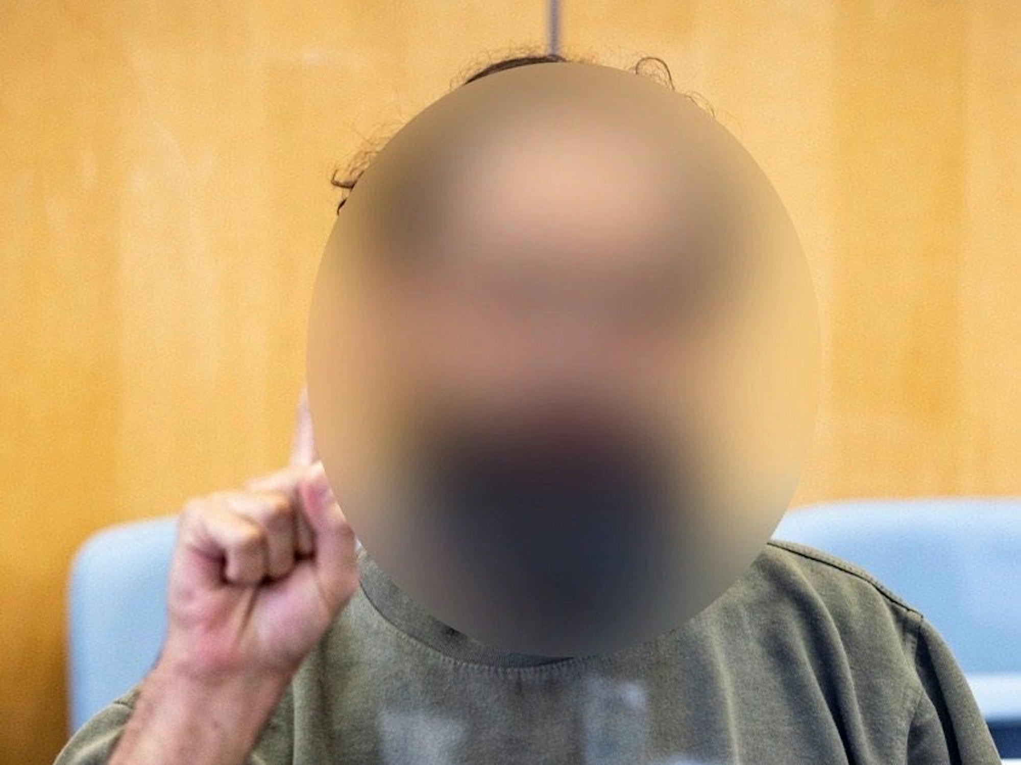 Der Angeklagte sitzt auf der Anklagebank hinter einer Glasscheibe, er zeigt dabei den Gruß der Kämpfer des IS, Tauhid.