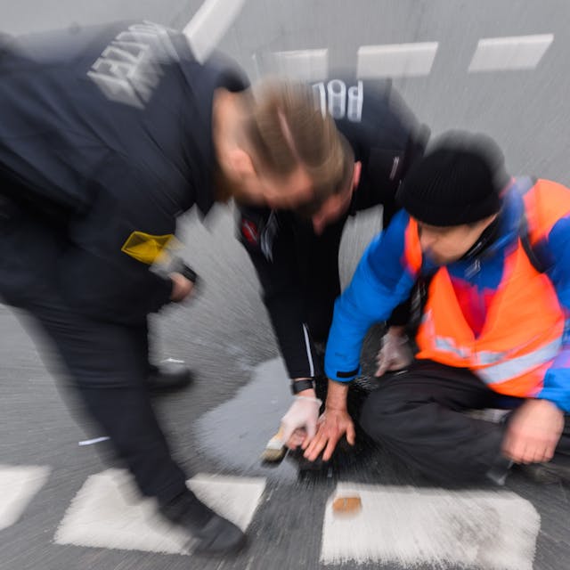 Polizisten versuchen festgeklebte Hände von Aktivisten der Gruppierung „Letzte Generation“ in Hannover mit Speiseöl von der Straße abzulösen.