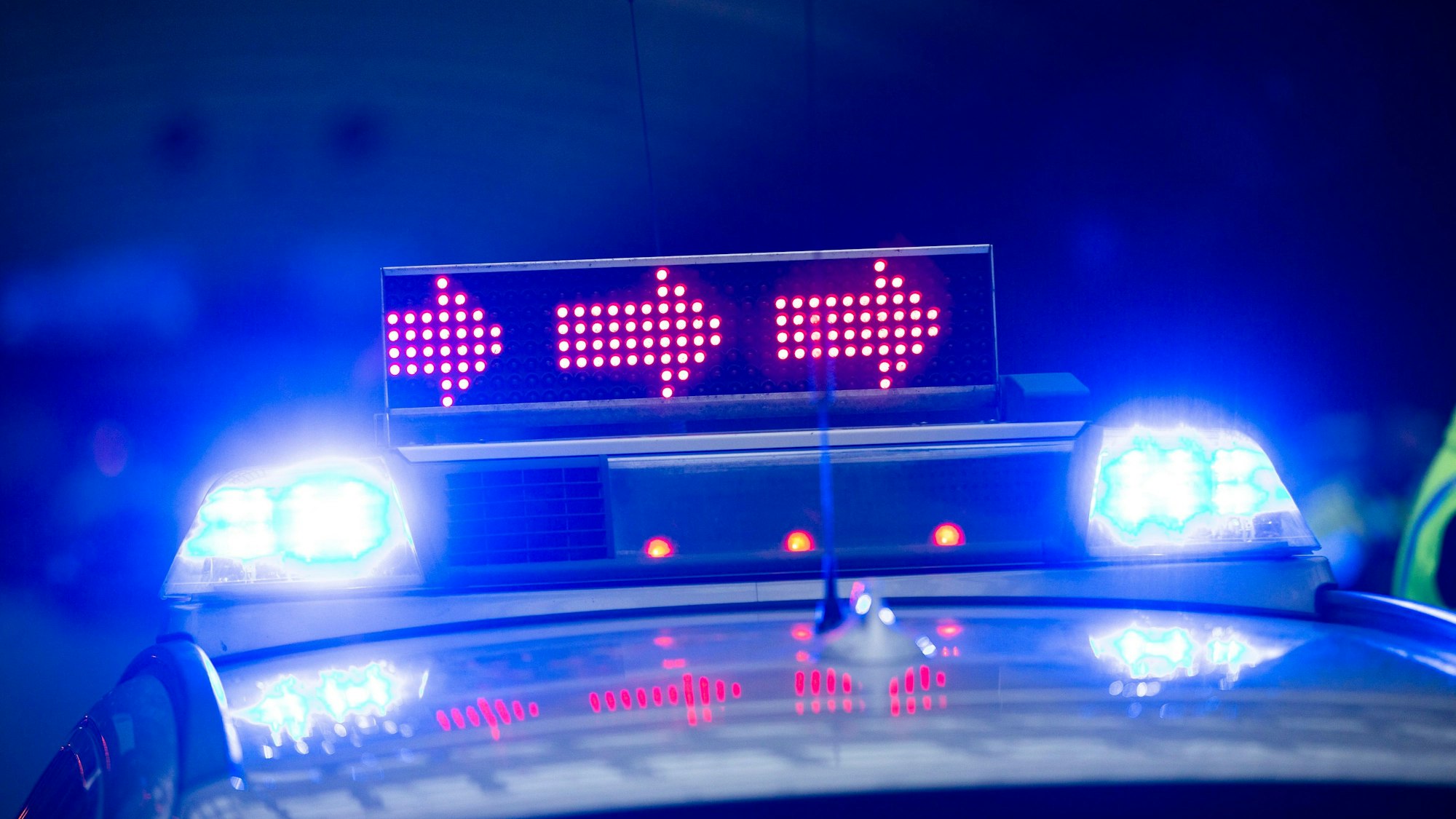 Auf einem Polizeiauto leuchtet das Blaulicht und rote Pfeile.
