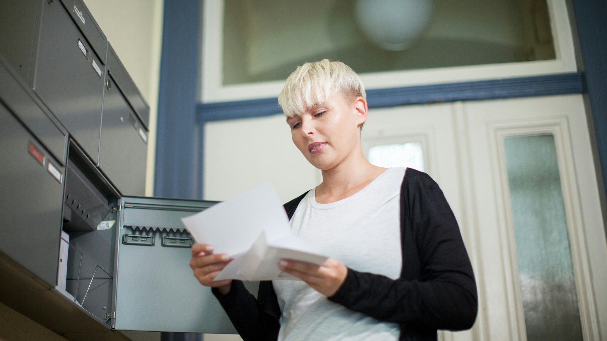 Eine Frau holt einen Brief aus ihrem Briefkasten im Hausflur