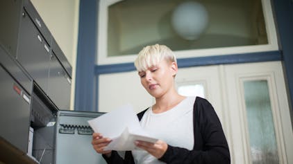 Eine Frau holt einen Brief aus ihrem Briefkasten im Hausflur