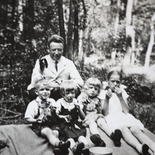 Edmund Schiefeling sitzt gemeinsam mit vier Kindern auf einer Decke beim Picknick im Wald.