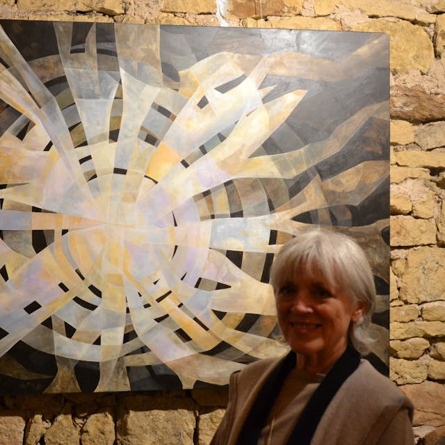 Gabriele Latzke steht vor einem Gemälde. Helle Streifen fließen von der Mitte des Bildes nach außen, der Hintergrund ist schwarz.