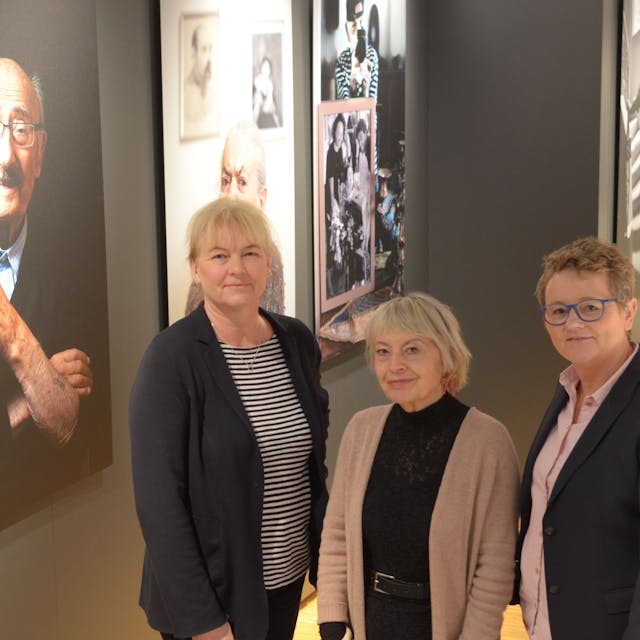 Dr. Heike  Lützenkirchen (l.) und Petra Goerge (r.) stellen im  Stadtmuseum Euskirchen mit Kuratorin Gisela Kayser die Sonderausstellung „Lonka Projekt“ vor. Sie stehen vor einer Reihe von Porträts von Holocaust-Überlebenden.