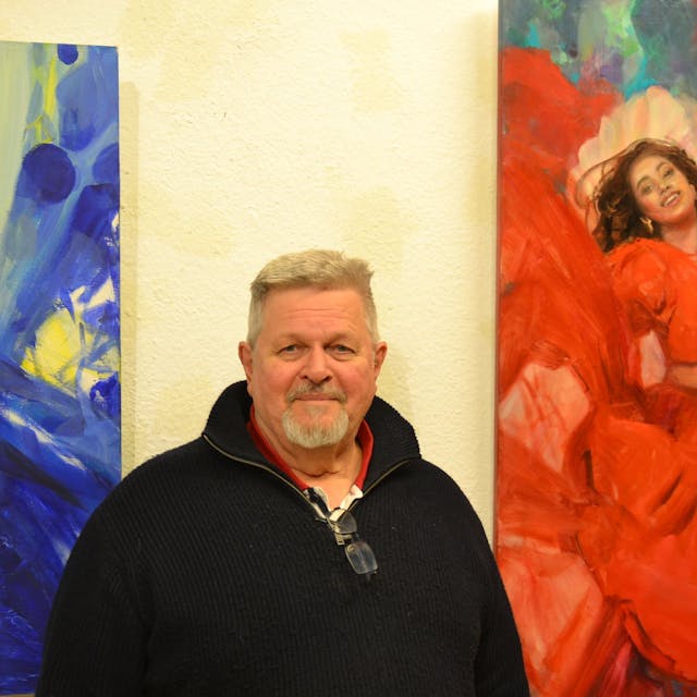 Galerist Rüdiger Axel Westphal steht vor einem Gemälde von Olga Müller, das eine Salsa-Tänzerin zeigt, deren rotes Kleid in ein Meer aus roten Blüten übergeht.