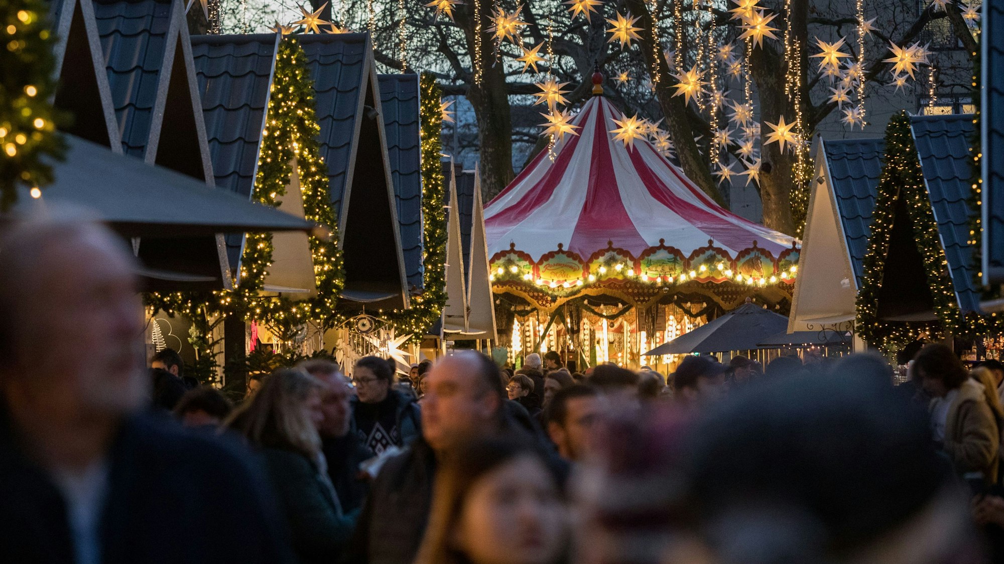 Besucher stehen dicht an dicht auf dem Weihnachtsmarkt. In den Bäumen hängen Sterne.