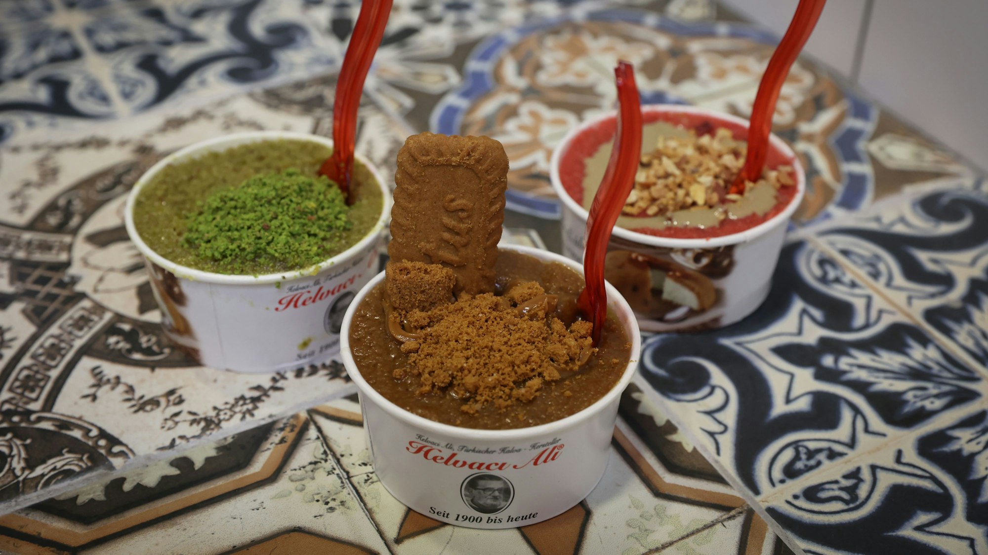 Drei Süßspeisen der türkischen Kette „Helvaci Ali“ stehen auf einem Tisch.