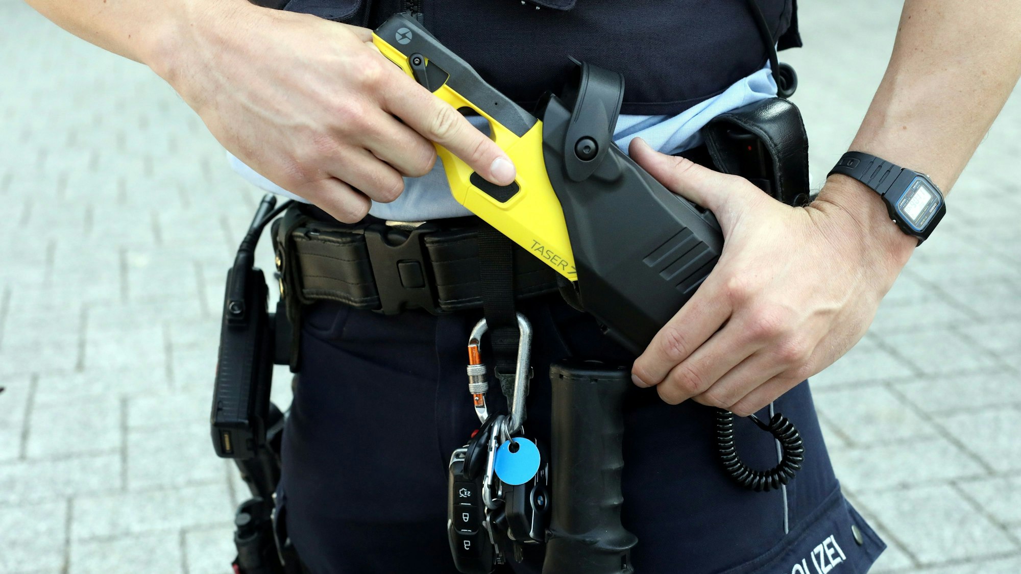 Ein Streifenpolizist zieht einen Taser aus der Halterung am Gürtel.